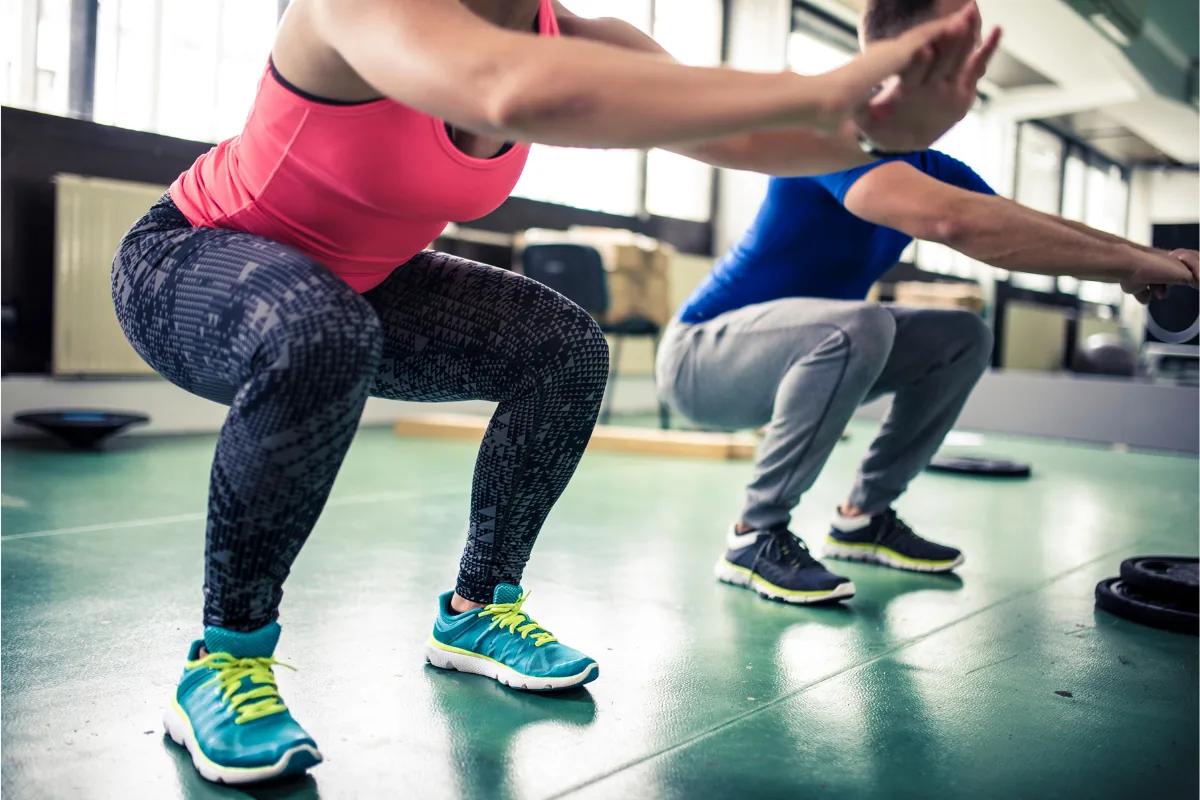 Two runners performing bodyweight squats in a gym