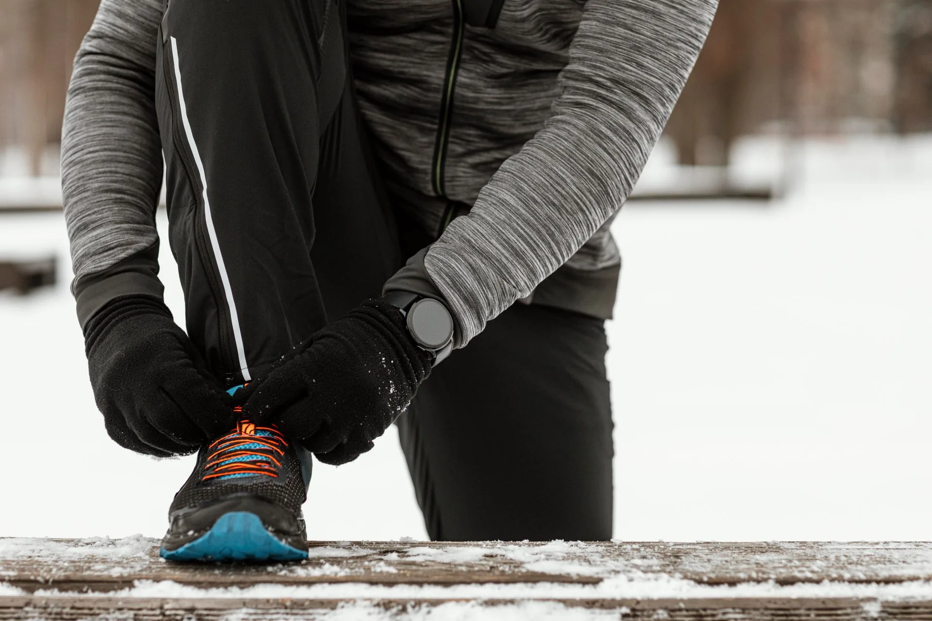Runner lacing up winter running shoes in the snow